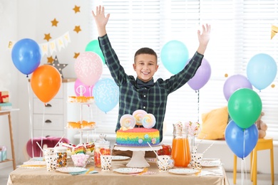 Photo of Happy boy at table with treats in room decorated for birthday party