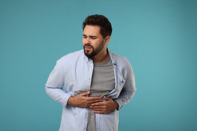 Photo of Young man suffering from stomach pain on light blue background