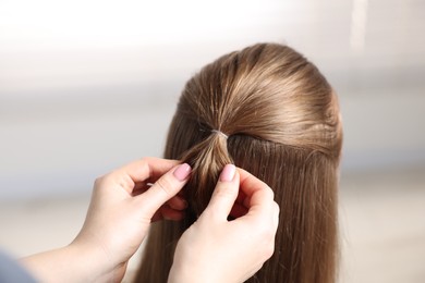 Professional stylist braiding woman's hair on blurred background, closeup