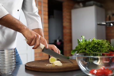 Photo of Professional chef cutting fresh leek in restaurant kitchen, closeup