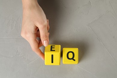 Woman turning cube with letters E and I near Q at light grey stone table, top view