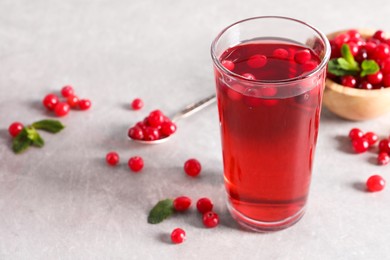 Photo of Tasty cranberry juice in glass and fresh berries on light grey table