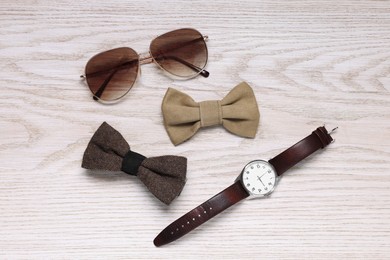 Photo of Stylish color bow ties, wristwatch and sunglasses on light wooden background, flat lay