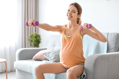 Photo of Young pregnant woman doing exercises with dumbbells at home