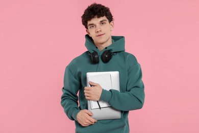 Portrait of student with laptop, notebook and headphones on pink background