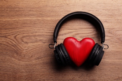 Photo of Decorative heart with modern headphones on wooden background, top view. Space for text