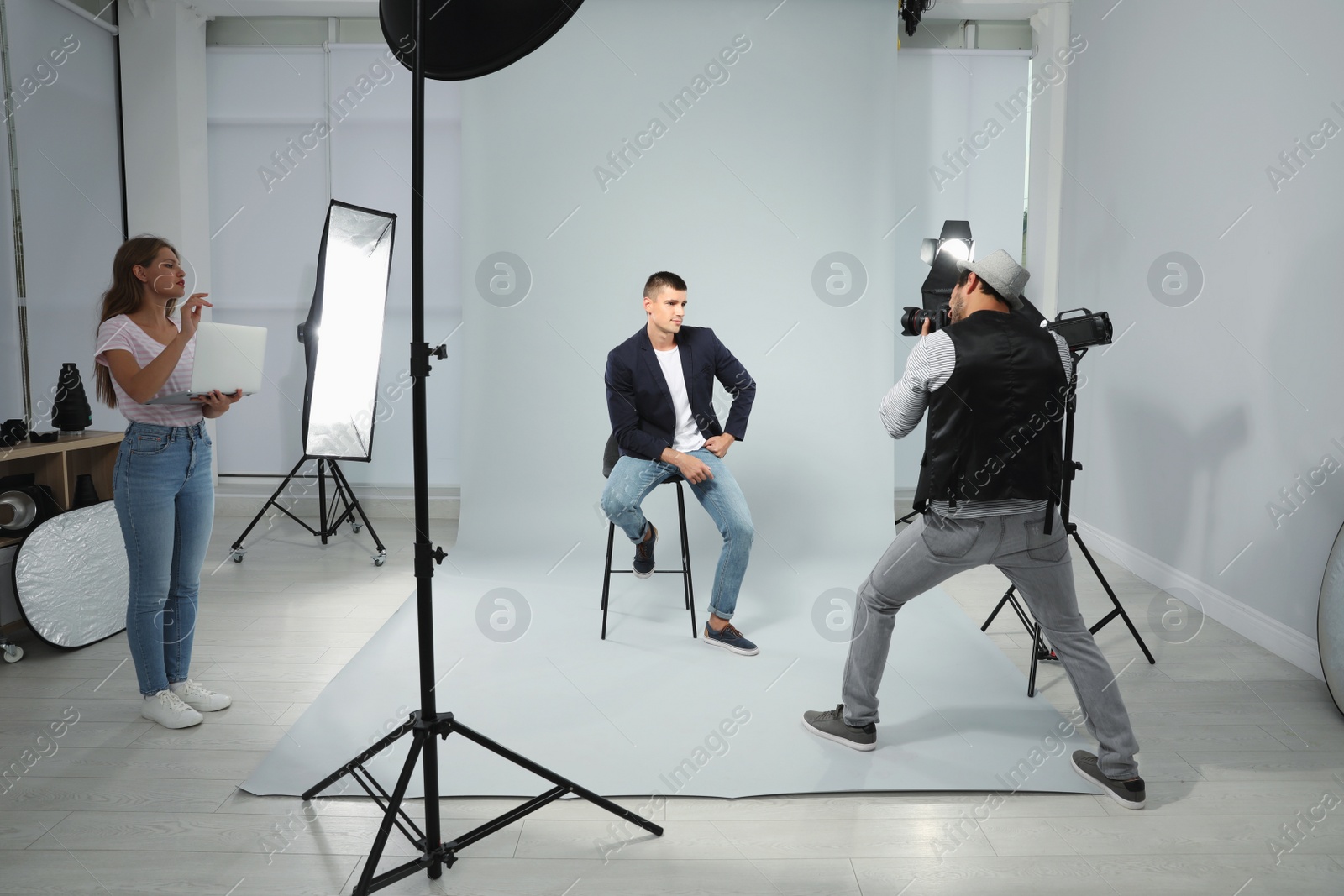 Photo of Professional photographer with assistant taking picture of young man in modern studio