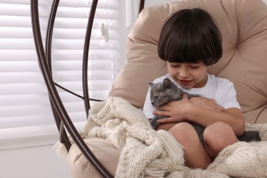 Cute little boy with kitten in hanging chair at home. Childhood pet