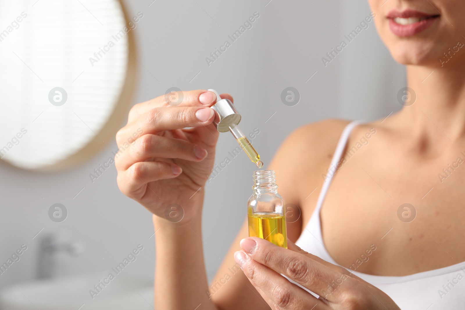 Photo of Woman with bottle of cosmetic serum on blurred background, closeup