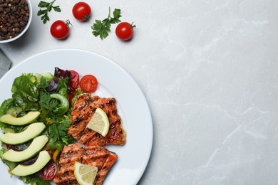 Photo of Tasty grilled salmon with avocado, lemon and tomatoes on light grey table, flat lay. Space for text