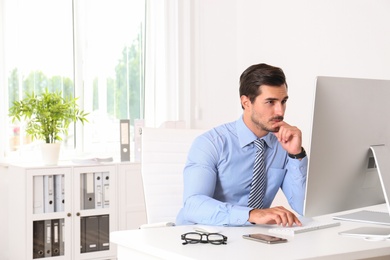 Photo of Handsome young man working with computer at table in office