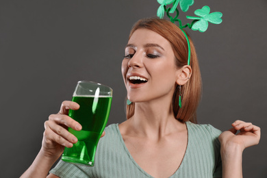 Photo of Young woman with clover headband and green beer on grey background. St. Patrick's Day celebration