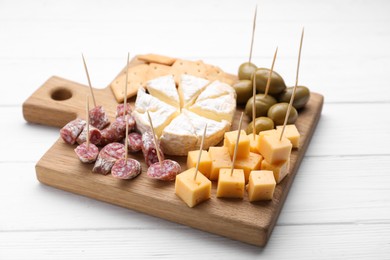 Photo of Toothpick appetizers. Pieces of sausage, cheese and olives on white wooden table