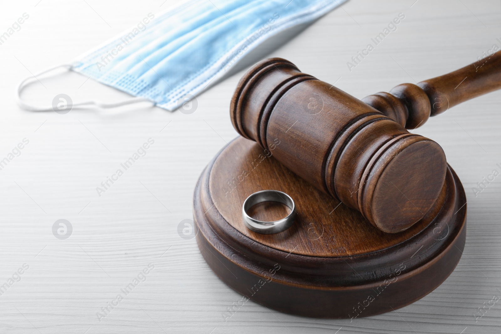 Photo of Gavel, wedding ring and protective mask on white wooden table. Divorce during coronavirus quarantine