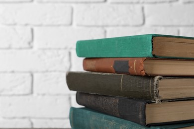 Photo of Many old hardcover books near white brick wall, closeup. Space for text