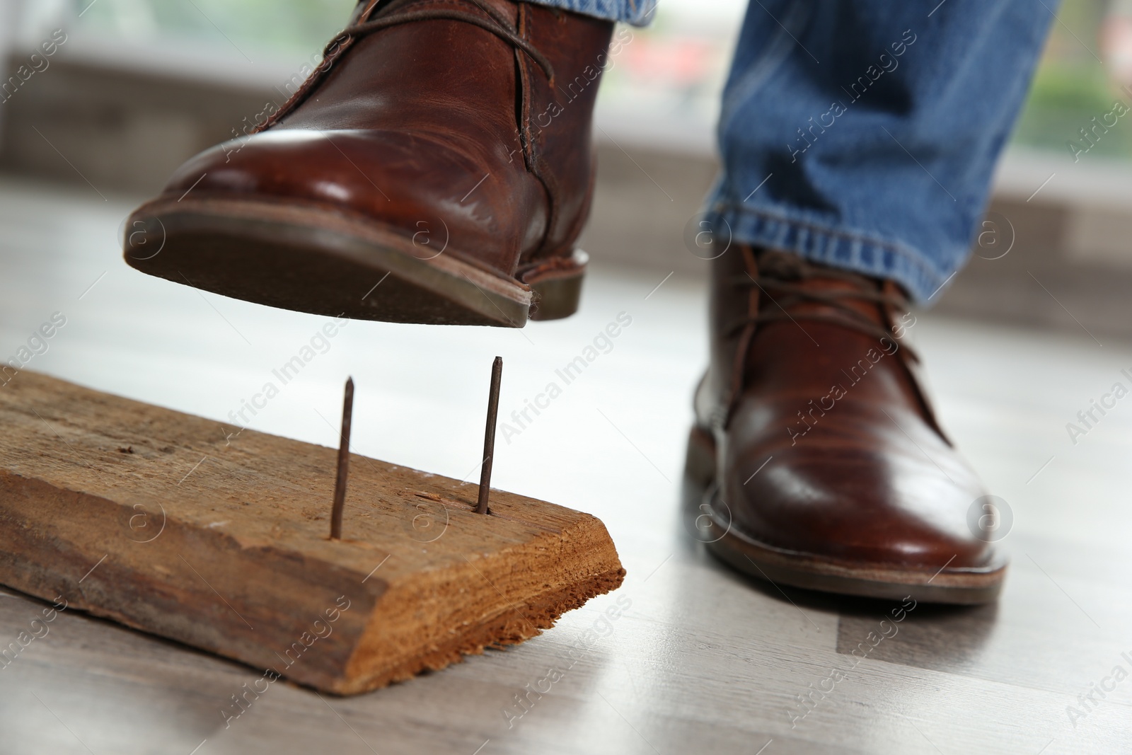 Photo of Careless man stepping on nails in wooden plank, closeup