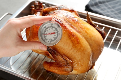 Photo of Woman measuring temperature of whole roasted turkey with meat thermometer, closeup