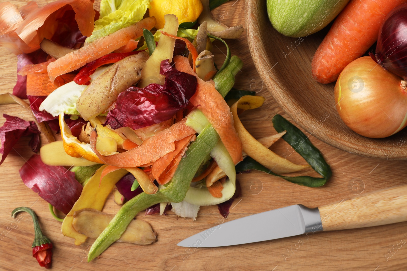 Photo of Different fresh vegetables with peels and knife on wooden table,top view