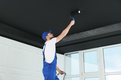 Worker in uniform painting ceiling with roller indoors