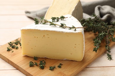 Board with pieces of tasty camembert cheese and thyme on light wooden table, closeup