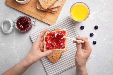 Photo of Woman spreading jam on toast against light background