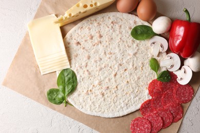 Pizza base and products on light textured table, top view