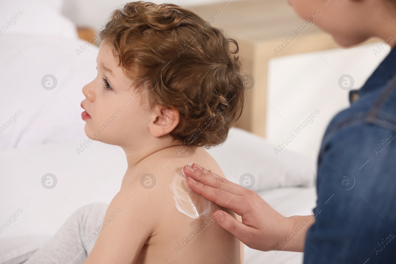 Photo of Mother applying ointment onto her son`s back on bed indoors