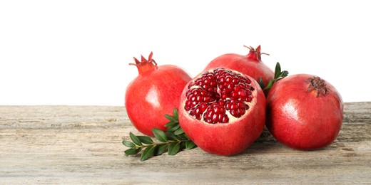 Fresh pomegranates and green leaves on wooden table against white background, space for text