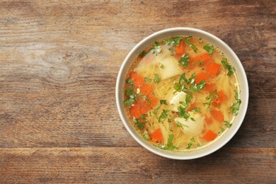 Photo of Bowl of fresh homemade chicken soup on wooden background, top view with space for text