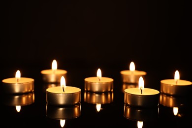 Photo of Burning candles on mirror surface in darkness, closeup