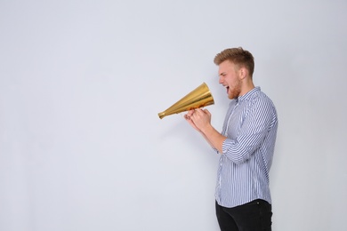Young man with megaphone on light background. Space for text