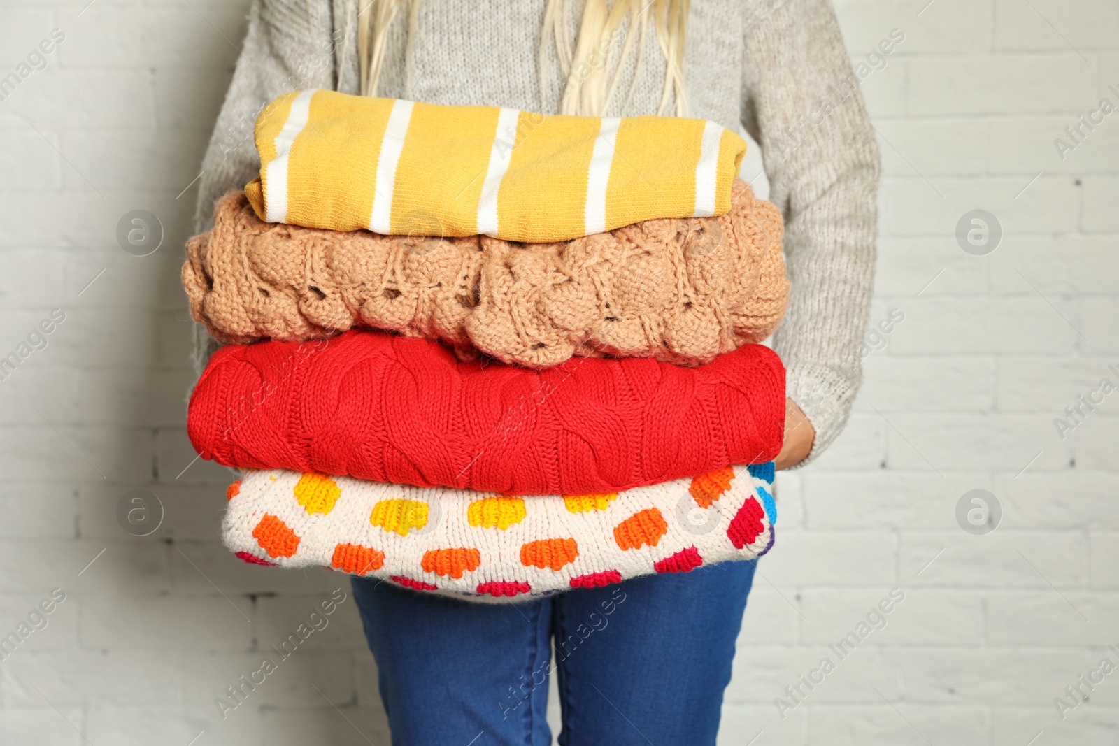 Photo of Woman holding stack of winter clothes against brick wall