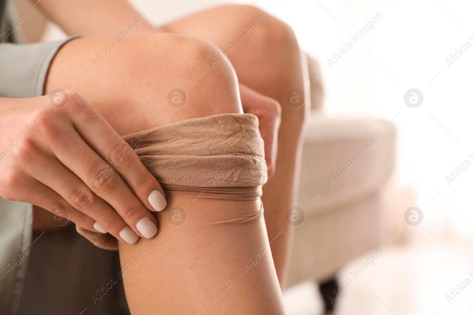 Photo of Beautiful woman putting on tights indoors, closeup