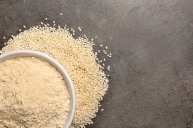 Photo of Bowl with sesame flour and seeds on grey background, top view. Space for text