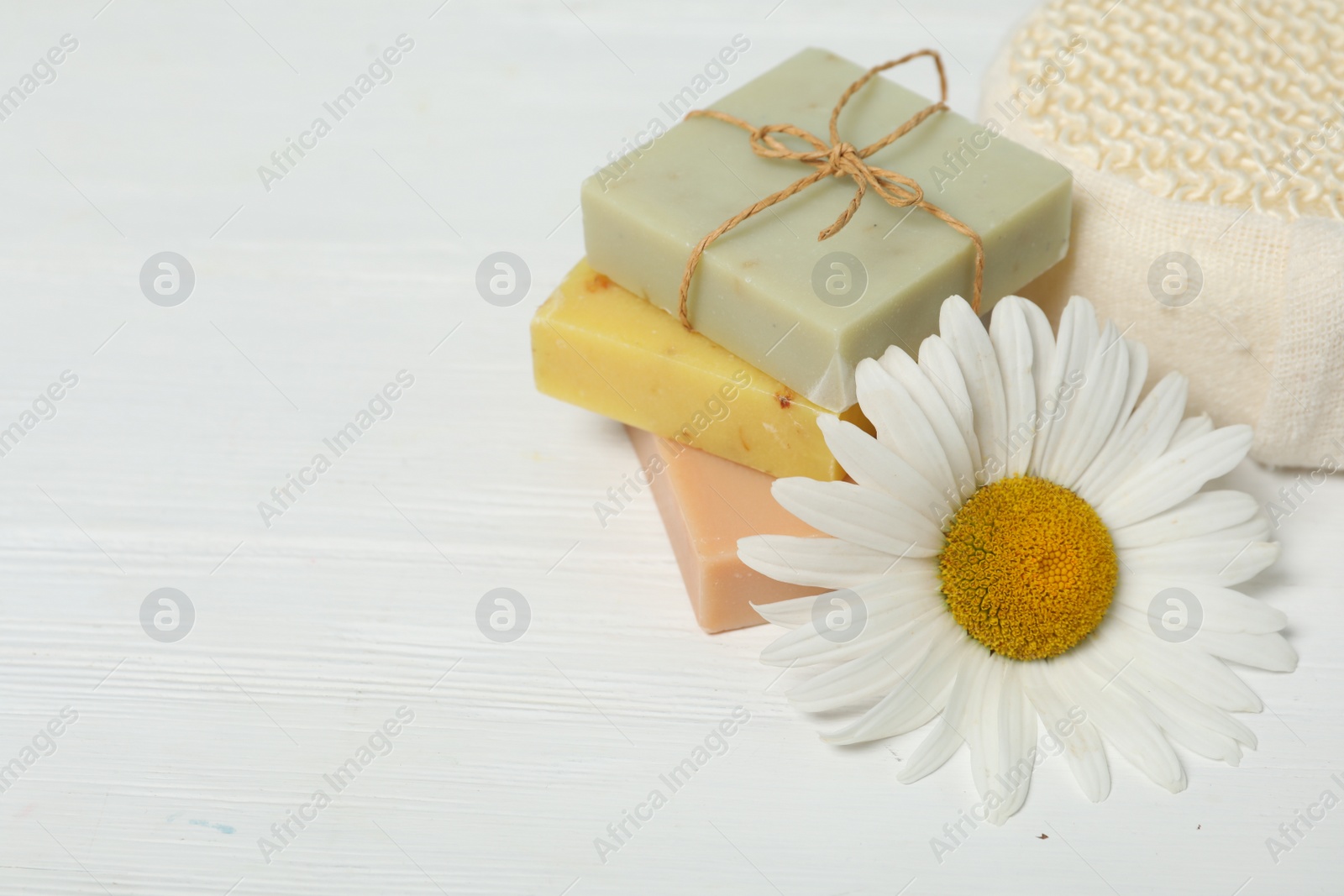 Photo of Bars of soap and and chamomile on white wooden table. Space for text