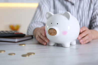 Photo of Woman with piggy bank at marble table indoors, closeup