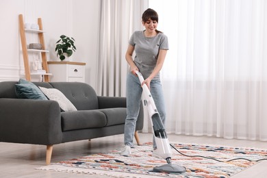 Happy young housewife vacuuming rug at home