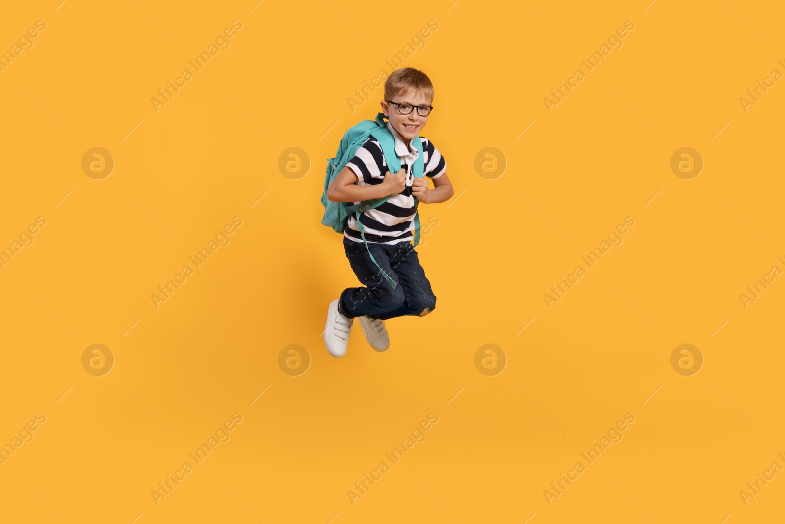 Photo of Happy schoolboy in glasses with backpack jumping on orange background