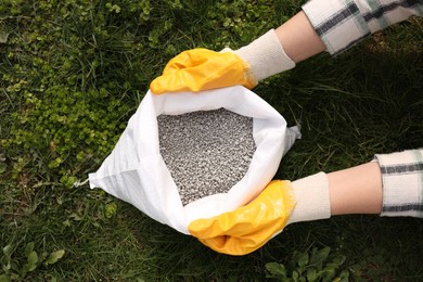 Woman with bag of fertilizer on green grass outdoors, top view