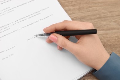 Woman signing document at wooden table, above view