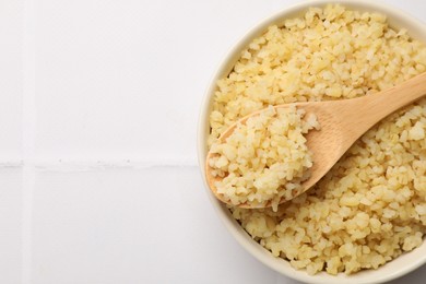 Photo of Delicious bulgur served on white tiled table, top view. Space for text