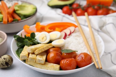 Delicious poke bowl with basil, vegetables, eggs and tofu on light grey table, closeup