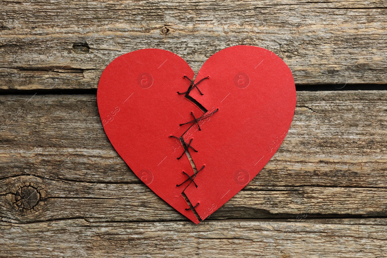 Photo of Broken heart. Torn red paper heart sewed with thread on wooden table, top view