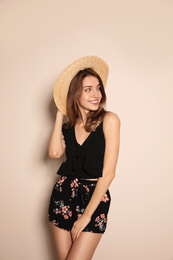 Photo of Young woman wearing floral print shorts and straw hat on beige background