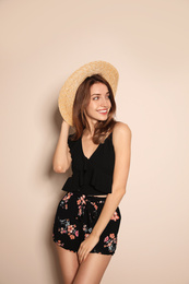 Young woman wearing floral print shorts and straw hat on beige background