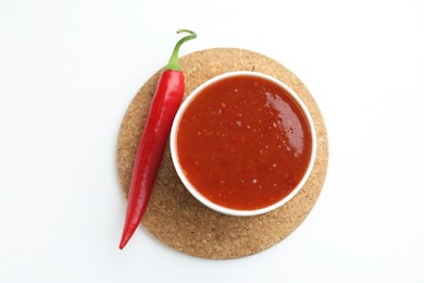 Photo of Spicy chili sauce in bowl and fresh pepper on white background, top view