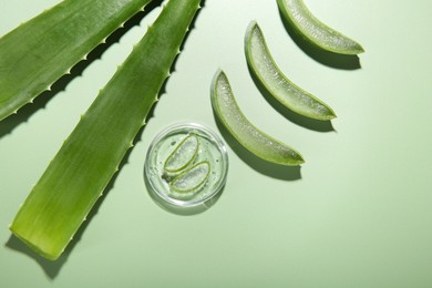 Photo of Cut aloe vera leaves and cosmetic gel on light green background, flat lay. Space for text