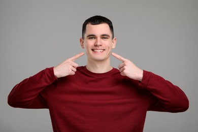 Photo of Man showing his clean teeth on grey background