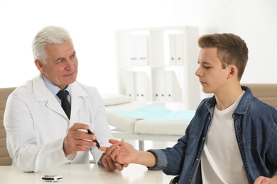 Doctor taking patient's blood sample with lancet pen in hospital. Diabetes control