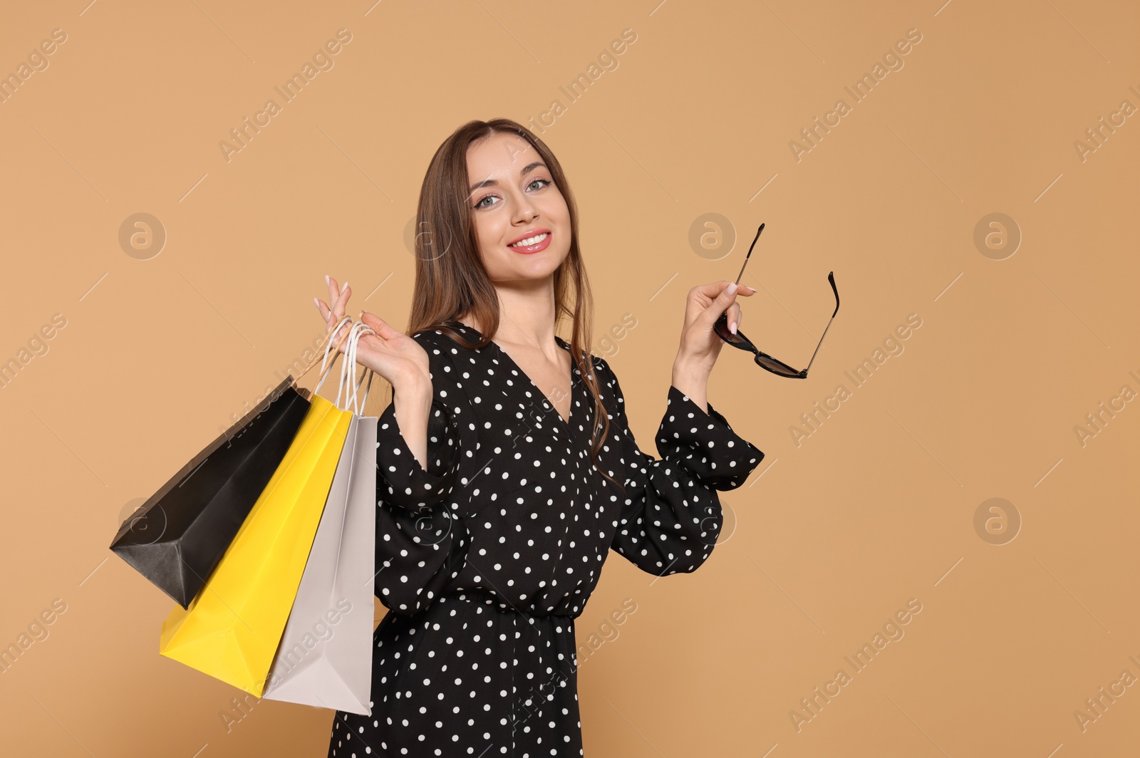 Photo of Stylish young woman with sunglasses and shopping bags on beige background